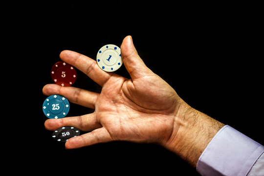 Multicolored poker chips with numbers placed between the fingers of a man's hand on a black background close-up - Powered by Adobe