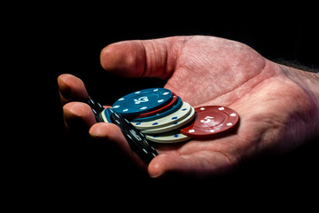 Multicolored poker chips lie in a man's hand on a black background close-up