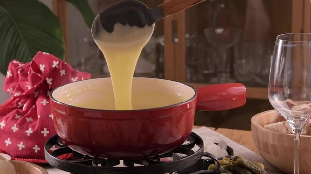 Cozy Swiss fondue setup with melted cheese, bread, pickles, and wine on a rustic table. advertising, social media campaigns, or food-related promotions. High quality 4k footage