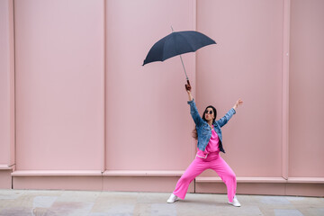 Young stylish woman holding umbrella and dancing in the street
