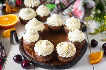 Cupcakes with vanilla cream on a wooden platter on a white table. Sweet dessert for breakfast. Close-up