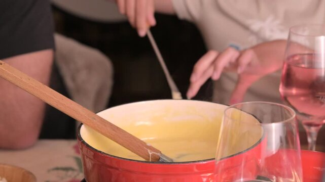 Cozy Swiss fondue setup with melted cheese, bread, pickles, and wine on a rustic table. advertising, social media campaigns, or food-related promotions. High quality 4k footage