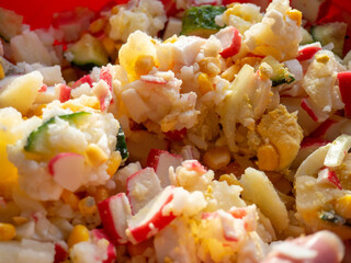 Making a salad with crab sticks. Many ingredients in the dish. Mixing the salad. Kitchen.