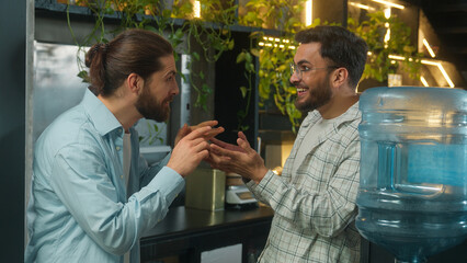 Arabian man drink water cooler in office coffee break pause two business men multiethnic businessmen colleagues coworkers Caucasian Indian guys friends talk secret gossip amazing news shock laughing
