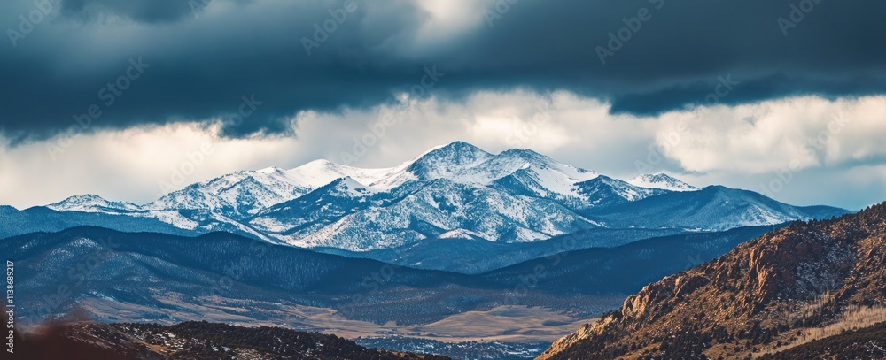 Poster snowy mountain range under cloudy skies viewed from a lower mountain range.