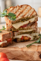 Grilled sandwich panini with mozzarella cheese, cherry tomatoes and pesto on wooden board, kitchen table background close up. Traditional italian food