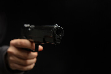 Hand holding a gun closeup, armed man on dark background. Danger and crime