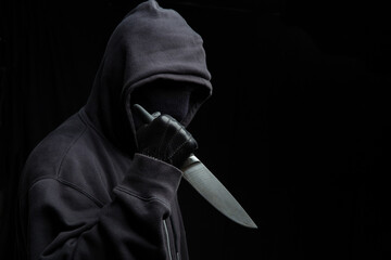 Criminal holding a knife, hooded man holding a weapon in gloved hand, armed attack concept.