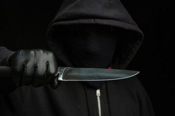 Criminal holding a knife, hooded man holding a weapon in gloved hand, armed attack concept.