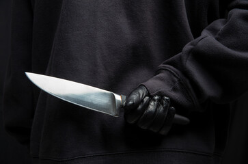Criminal hiding a knife behind his back, man holding a weapon in gloved hand closeup