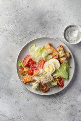Caesar salad with chicken meat, green iceberg salad, eggs, tomatoes and Parmesan on gray background isolated. Top view, flat lay