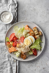 Caesar salad with chicken meat, green iceberg salad, eggs, tomatoes and parmesan cheese on gray background. Top view, flat lay