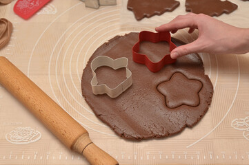 Christmas homemade baking, woman hand cuts out dough for baking gingerbread, cutter, rolling pin, spatula on the table
