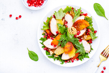 Winter persimmon salad with grilled chicken, pomegranate, walnuts, oranges and lettuce, white background, top view