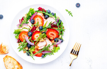 Foodie food salad with strawberry, grilled chicken, arugula, blueberries and walnuts with ciabatta, white table., top view