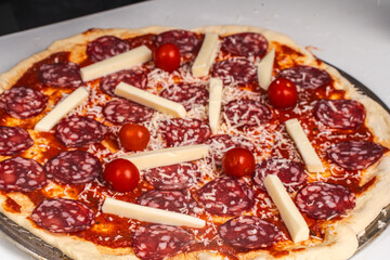 Pizza is prepared for baking. Raw pepperoni pizza with sausage, mozzarella cheese, cherry tomatoes and basil on a baking wheel