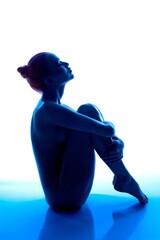 Silhouette of a woman sitting gracefully with blue lighting backdrop © Wisky