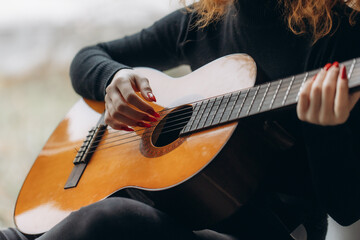 A redheaded woman holds music and plays the guitar