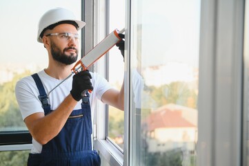 Worker sealing plastic window with caulk indoors. Installation process
