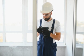 Workman in overalls installing or adjusting plastic windows in the living room at home