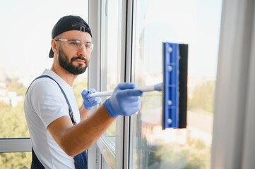 Caucasian handsome man, worker of cleaning service, in blue overalls and in a cap, blaser, Cleaning, washing Windows by special mop, enjoying his work. High quality photo