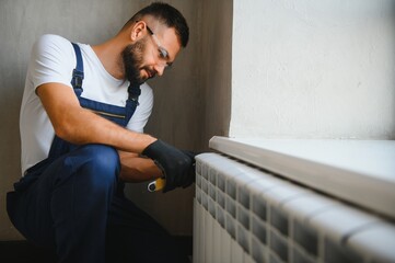 A plumber is fixing a radiator. With an adjustable wrench, he tightens the tap