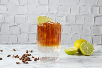 Refreshing espresso tonic drink with lime and coffee beans on white marble table