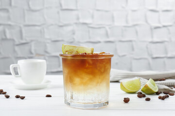 Refreshing espresso tonic drink with slice of lime and coffee beans on white wooden table
