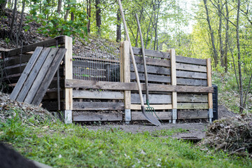 Homemade DIY compost bin made from wooden pallets in a vegetable garden with tools nearby / Concept: sustainable waste recycling, permaculture