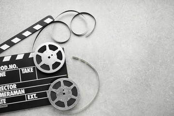 Movie clapper and film reels on grey textured table, top view. Space for text