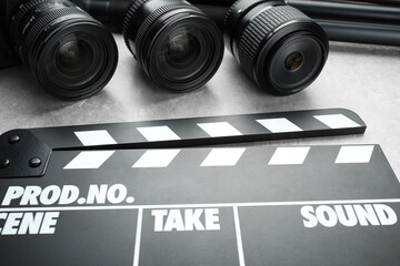 Movie clapper and camera lens on grey table, closeup