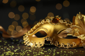 Beautiful carnival mask and confetti on dark background with blurred lights, closeup