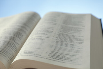 Open Holy Bible in English language on light blue background, closeup