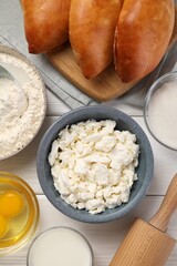 Delicious pirozhki (stuffed pastry pies) and ingredients on white wooden table, flat lay