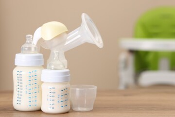 Feeding bottles with milk and breast pump on wooden table indoors, space for text