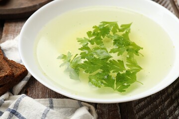 Tasty chicken bouillon with parsley in bowl on wooden table, closeup
