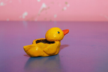 yellow duck made of polymer clay on a blue table in the form of a pot of soil with an orange beak...