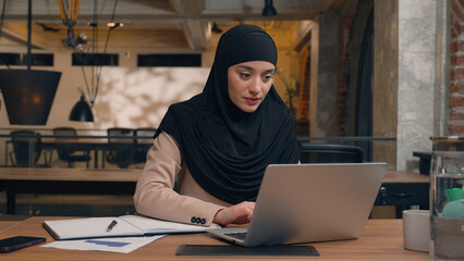 Muslim woman in hijab female worker freelancer student Arabian businesswoman employee office manager agent online laptop remote work at workplace using computer pc smiling islamic girl business lady