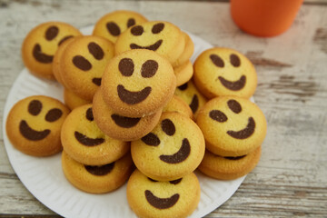 Yellow cookies shaped like smiling emojis are stacked on a white plate in close-up, good mood,...