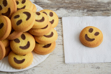 Yellow cookies shaped like smiling emojis are stacked on a white plate, with one cookie on a napkin nearby in close-up, leadership qualities, the life of the party
