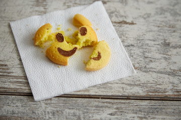 A broken cookie shaped like a smiling emoji on a paper napkin in close-up, spoiled mood, complex emotions, end of the holidays, conclusion of the party.