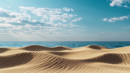 This image captures serene sandy dunes gently sloping towards a calm and vast blue sea under a bright and cloud-dotted sky, evoking tranquility and wanderlust.