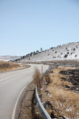 An empty road through snowy mountains and peaks with snow under a blue sky with sun shining