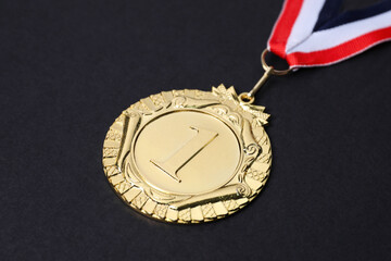 Golden medal with striped ribbon on black background, closeup