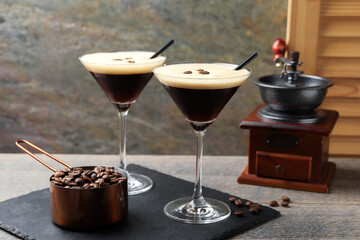Glasses of delicious espresso martini, manual coffee grinder and beans on wooden table