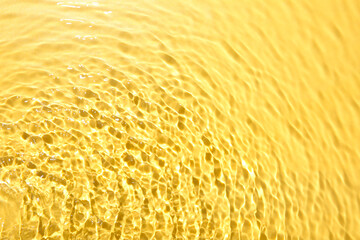 Rippled surface of clear water on yellow background, closeup
