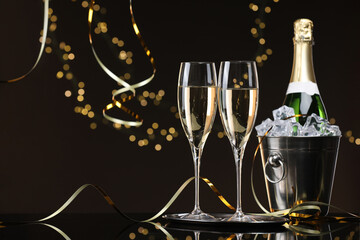 Champagne and bucket of ice on mirror surface against brown background with blurred lights, space for text