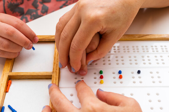 The hands of a girl and the hands of a teacher in close-up. Braille board for learning alphabet