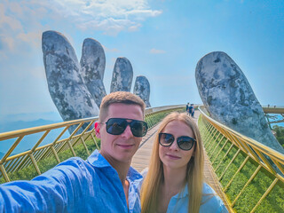 Young European couple models posing on a Golden Bridge in Ba Na hills, Da Nang, Vietnam on a sunny day. Iconic world famous bridge in the mountains