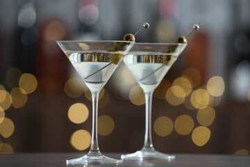 Martini cocktail with olives in glasses on wooden table against blurred background, closeup. Bokeh effect